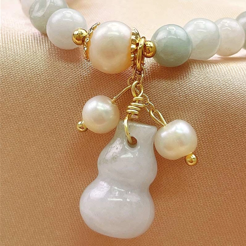 Close-up detail of polished jade beads, freshwater pearls, and carved gourd charm with gold wrapping