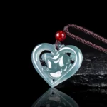 Icy blue jade love heart rabbit pendant with hollow carved design, shown from left side overhead angle with brown waxed cord and red bead accent on dark reflective studio background
