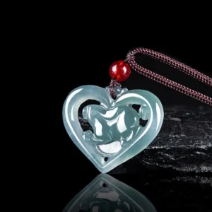 Icy blue jade love heart rabbit pendant with hollow carved design, shown from left side overhead angle with brown waxed cord and red bead accent on dark reflective studio background