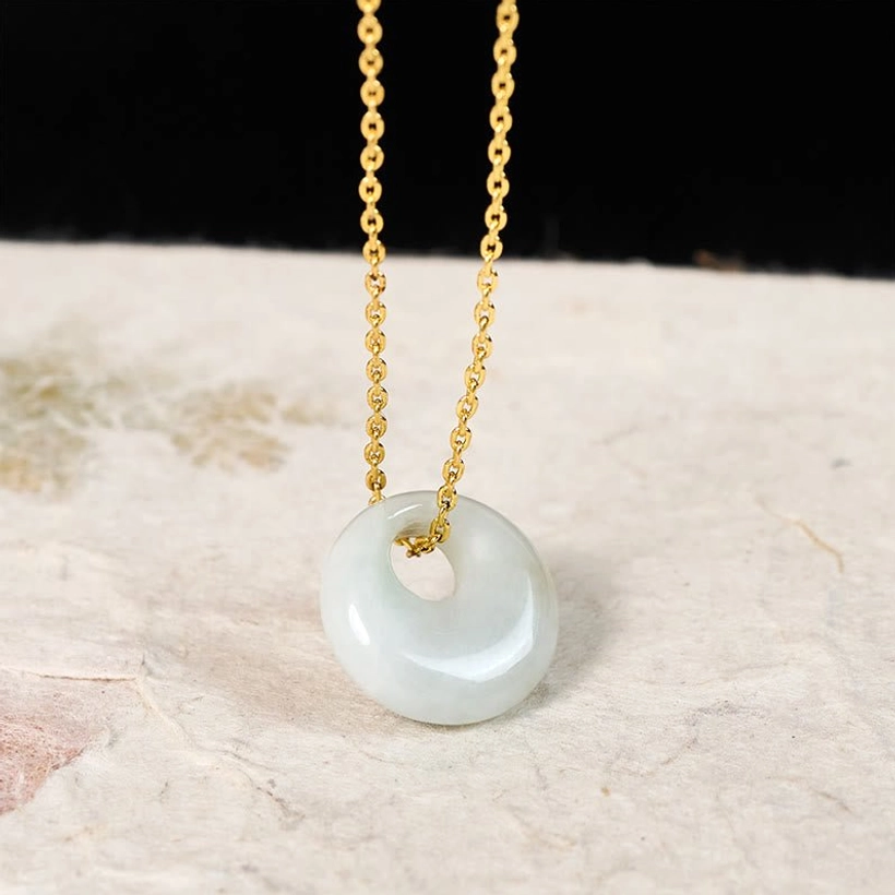 Mini jade pendant hanging on gold chain against vintage paper background, front view