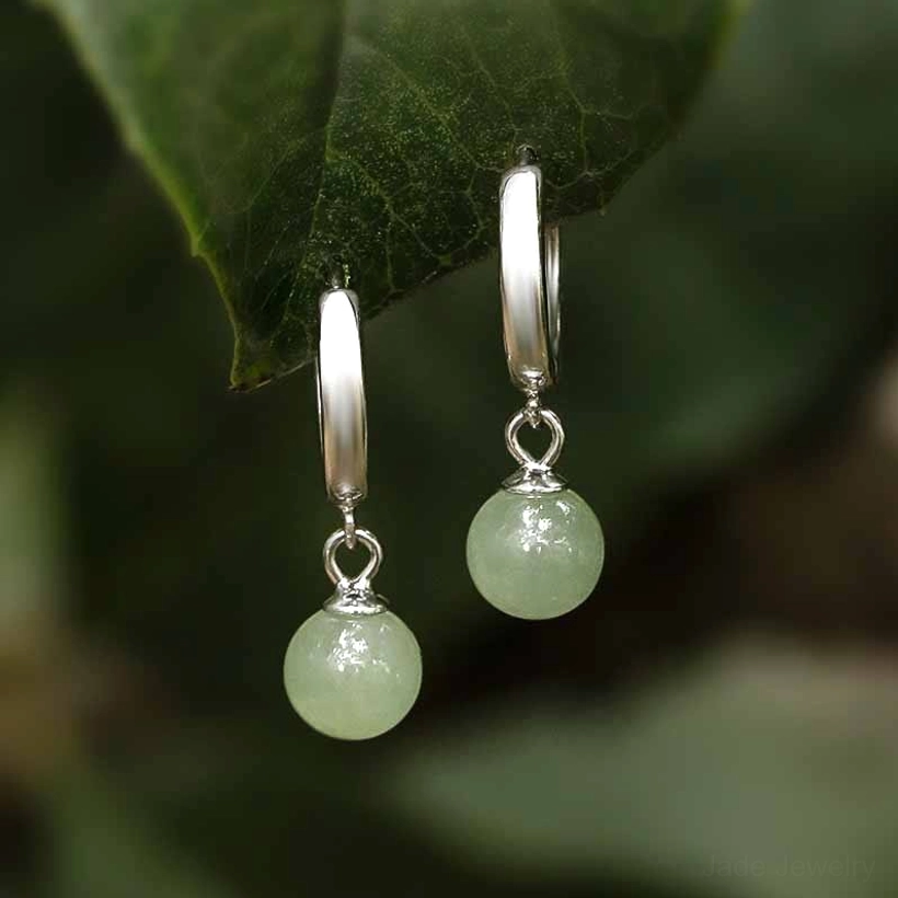 Polished sterling silver jade bead earrings side view with dangling light green jade charms, outdoor foliage setting