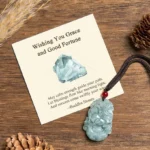 Jade horse pendant necklace with red cord and protective bead on wooden surface with pinecones, flat lay showing greeting card included