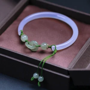 Pale purple-white jade bangle with dangling jade pendants and green cord, displayed on burgundy velvet pad with wooden tray