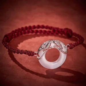 Koi fish jade bracelet side angle showing silver ornament and maroon braided cord against dark background