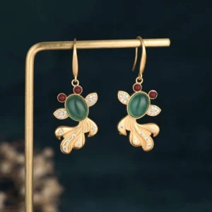 Hanging jade koi fortune earrings displaying gold ear hooks, green jade center stone, and red gem accents in koi tail design