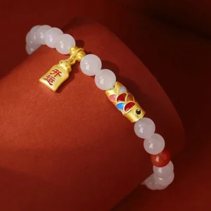 Koi fish fortune bracelet with white jade beads, red agate accents, and gilt silver koi ornament on red velvet background, oblique angle