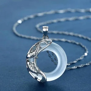 Close-up three-quarter view of white jade koi pendant showing intricate silver koi carving detail and translucent jade properties on dark blue background