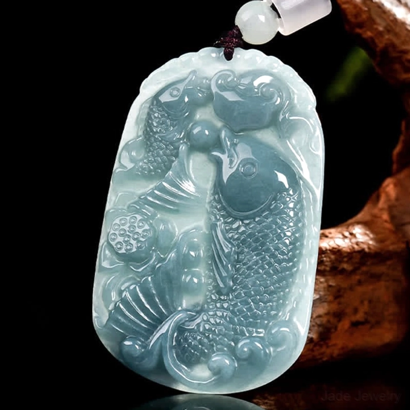 Double koi fish jade pendant three-quarter front angle view on wooden decorative stand, displaying master carving craftsmanship and detailed fish relief with beaded hanging loop
