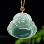 Natural teal jade Laughing Buddha pendant necklace with 18K gold clasp on dark green foliage background