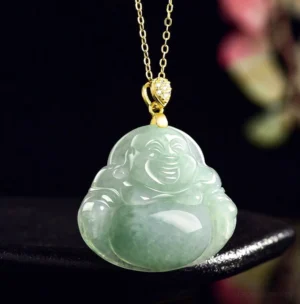 Jade laughing Buddha necklace on black display stand with floral arrangement, three-quarter angle showcasing mottled light green jadeite and gold jewelry bail