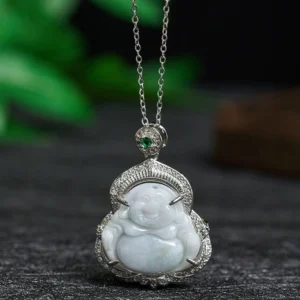 Pale light-green jade Laughing Buddha pendant necklace with silver filigree setting, displayed overhead on dark desktop with green leaf decor