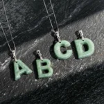 Collection of jade letter pendants A B C D with 925 sterling silver chains on dark slate display