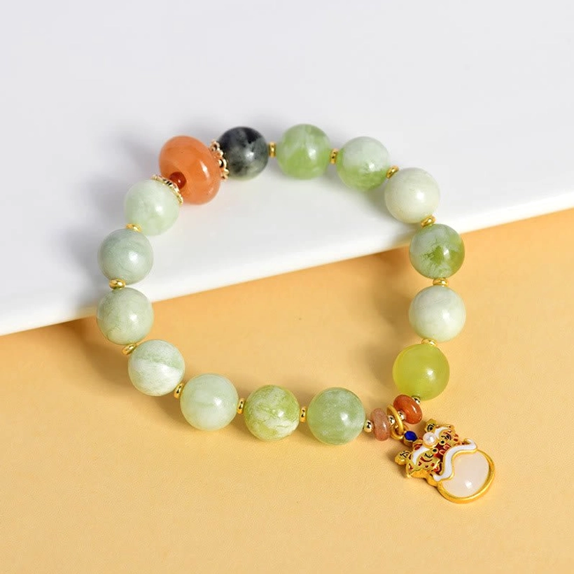 Jade dancing lion bracelet side angle showing gold enamel lion charm and mixed natural jade beads on table