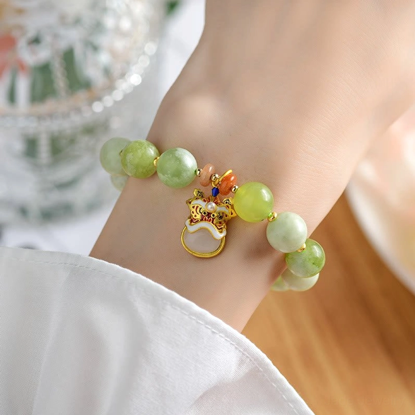 Close-up of jade dancing lion bracelet worn on hand showing enamel lion charm and gradient green beads with glass decor