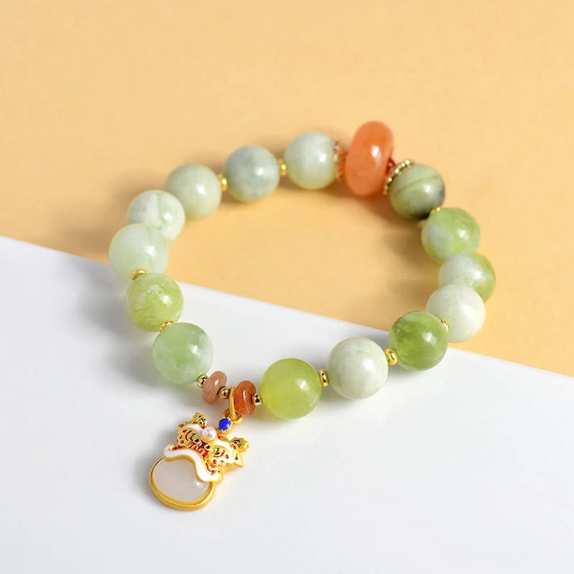 Jade dancing lion bracelet side view on light yellow background showing gradient green beads and gold enamel lion pendant