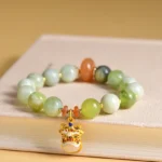 Natural jade dancing lion charm bracelet displayed on hardcover book with mixed green and orange accent beads
