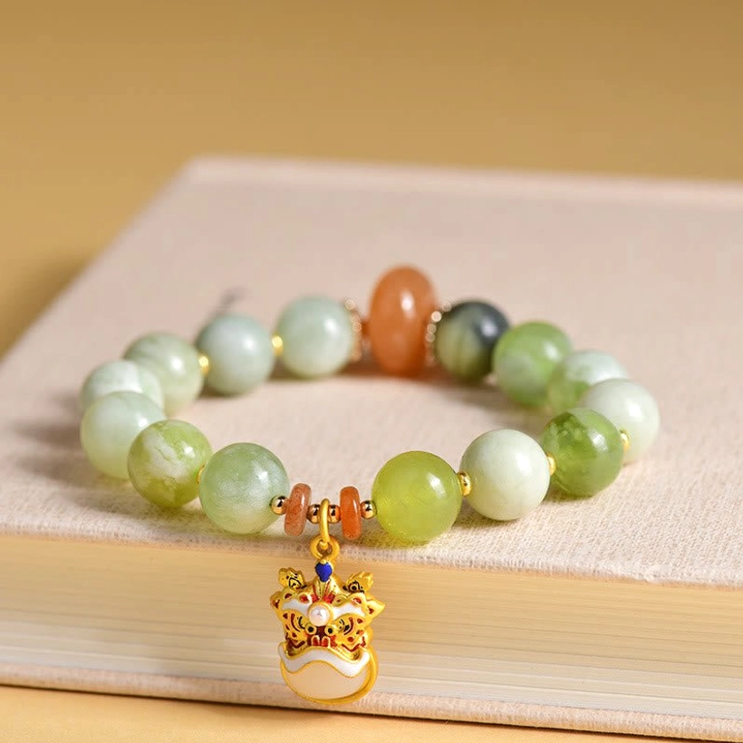 Natural jade dancing lion charm bracelet displayed on hardcover book with mixed green and orange accent beads
