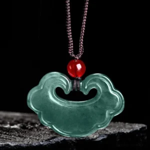 Green jade Chinese lock charm pendant flat lay on black background displaying red bead accent and brown cord detail