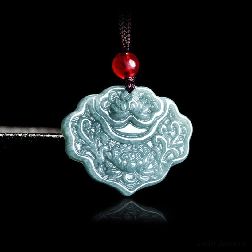 Natural celadon jade longevity lock pendant with lotus and floral carvings against dark background