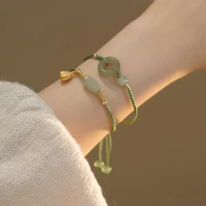 Green jade string bracelets with lotus pendant and gold charm worn on wrist, paired with beige knit sleeve, demonstrating adjustable fit