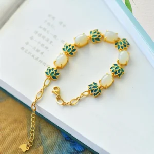 Lotus jade bracelet with adjustable extender chain displayed on open book, featuring gold hardware and matched jade enamel decoration, side flat lay view