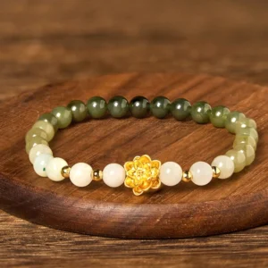 Circular Hetian jade lotus bracelet flat lay on wooden coaster, displaying full beaded strand with white and green jade gradient and gold lotus center