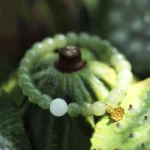 Green jade beaded bracelet with white accent bead and gold lotus pendant, displayed overhead on green lotus pod