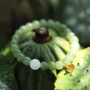 Green jade beaded bracelet with white accent bead and gold lotus pendant, displayed overhead on green lotus pod