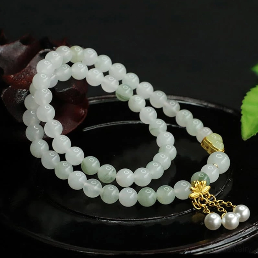 Handcrafted Tianshan jade double-loop bracelet with light green beads, gold clasp, and pearl tassel on dark wooden background