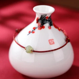 Premium hetian jade lotus bracelet displayed with plum blossom porcelain and red satin backdrop, showing detailed carving