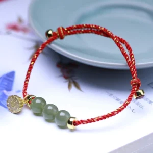 Red jade lotus seed bracelet with gold charm on ceramic plate - adjustable jade beads woven with red cord