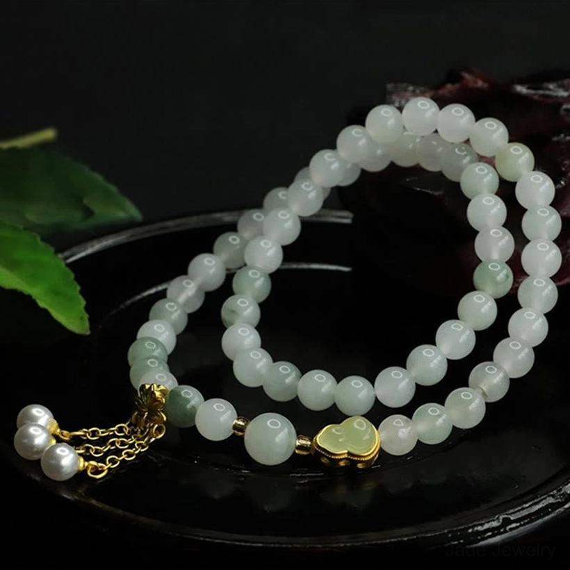 Tianshan jade bracelet side view with matte round jade beads, gold clasp, and pearl tassel charm against natural background