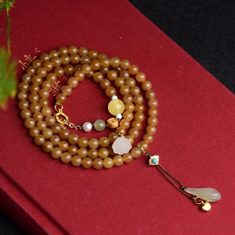 Close-up of jade beaded bracelet with white lotus charm, gold clasp, and turquoise pendant on red satin