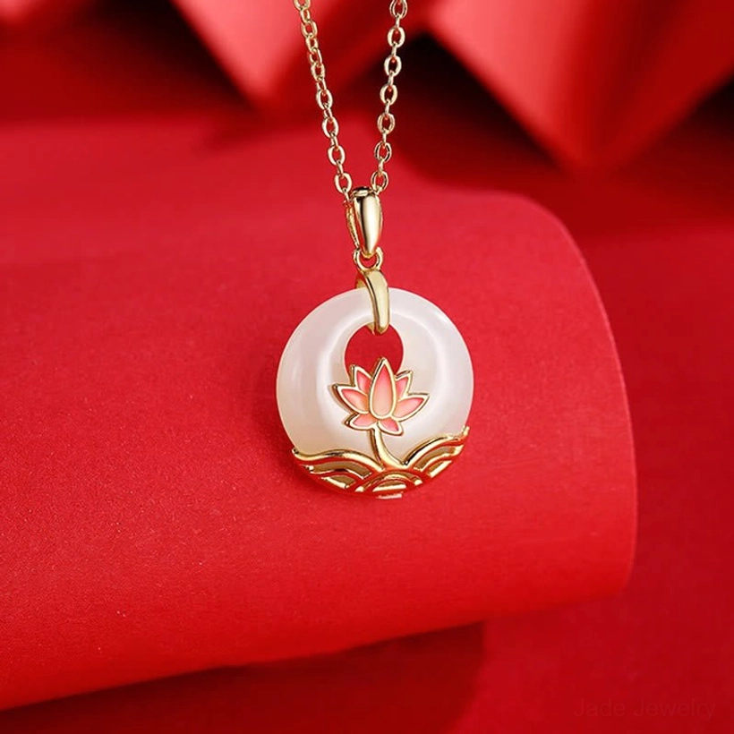 White jade lotus necklace close-up detail showing enamel lotus base and jade donut stone with gold-toned metal on red fabric