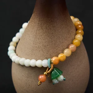 Natural jade quartzite beaded bracelet with green lotus peace buckle charm displayed alongside ceramic vase, showing gradient yellow and white stone beads