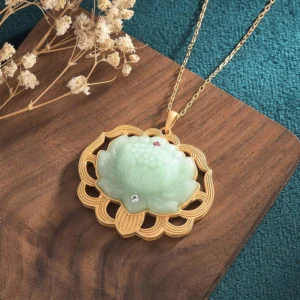 Handcrafted jade lotus pendant showing carved details, textured gold frame, and pink and clear gem accents from overhead angle