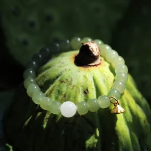 Dark green jade bead bracelet featuring white accent bead and ornate gold lotus charm resting on botanical lotus pod