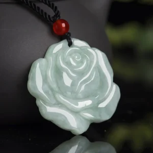 Light green hand-carved jade lotus rose pendant with black braided cord and red agate bead, overhead close-up view on reflective background