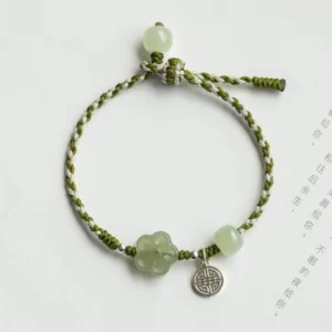 Jade prosperity bracelet flat lay showing two-tone green braided cord with carved jade flower beads and silver longevity pendant