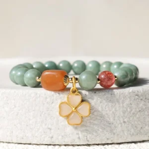Jade prosperity bracelet flat lay on stone display featuring round green jade beads and gold four-leaf clover charm
