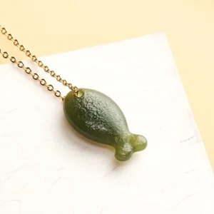 Deep green Hetian jade fish charm necklace overhead view on white background, showcasing textured matte finish and connected chain link