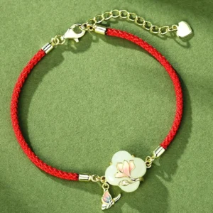 Flat lay overhead view of clover-shaped jade charm with pink enamel magnolia flower and butterfly accent