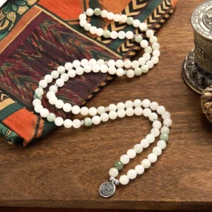 Loose natural Tianshan jade prayer beads scattered on embroidered fabric and wooden table, displaying authentic white and pale green round meditation beads with silver lotus charm