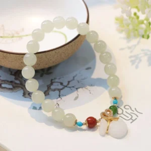 Side view of white jade prosperity bracelet with gold-plated pendant charm beside ceramic bowl