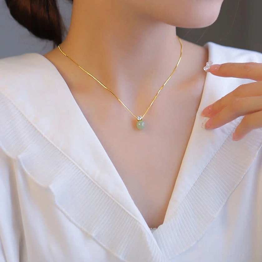 Side view of jade prosperity pendant necklace resting at collarbone with delicate gold chain on white ruffled shirt