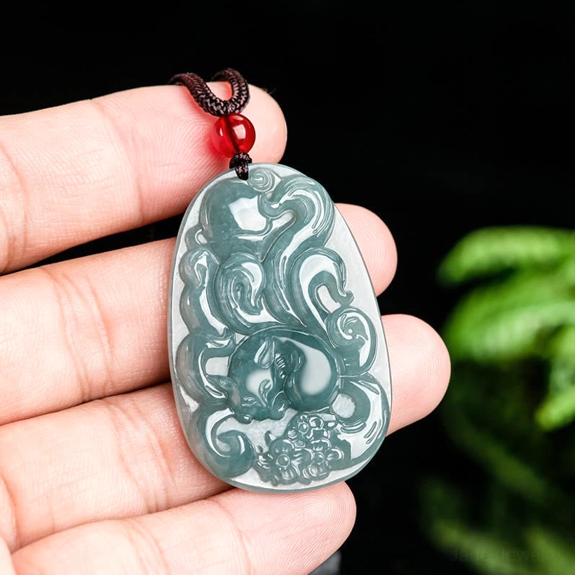Hand-held view of light jade nine-tailed fox pendant necklace showing scale on human hand with detailed carving