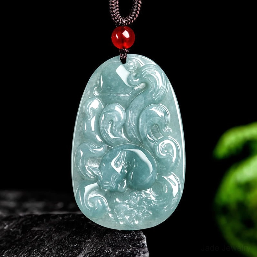 Light cyan jade nine-tailed fox pendant necklace overhead flat lay view, showing intricate carved relief work with red auspicious bead and brown cord