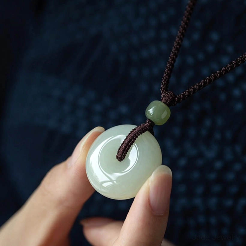 Jade peace buckle pendant held on fingertip showing glossy green surface spacer bead and craftsmanship detail