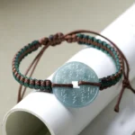Natural jade peace buckle bracelet with adjustable woven cord, displayed in oblique top-down view