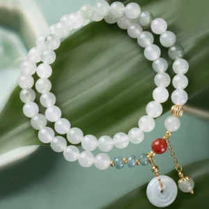 Green jade peace buckle double wrap bracelet flat lay on leaf backdrop with red agate and gold hardware